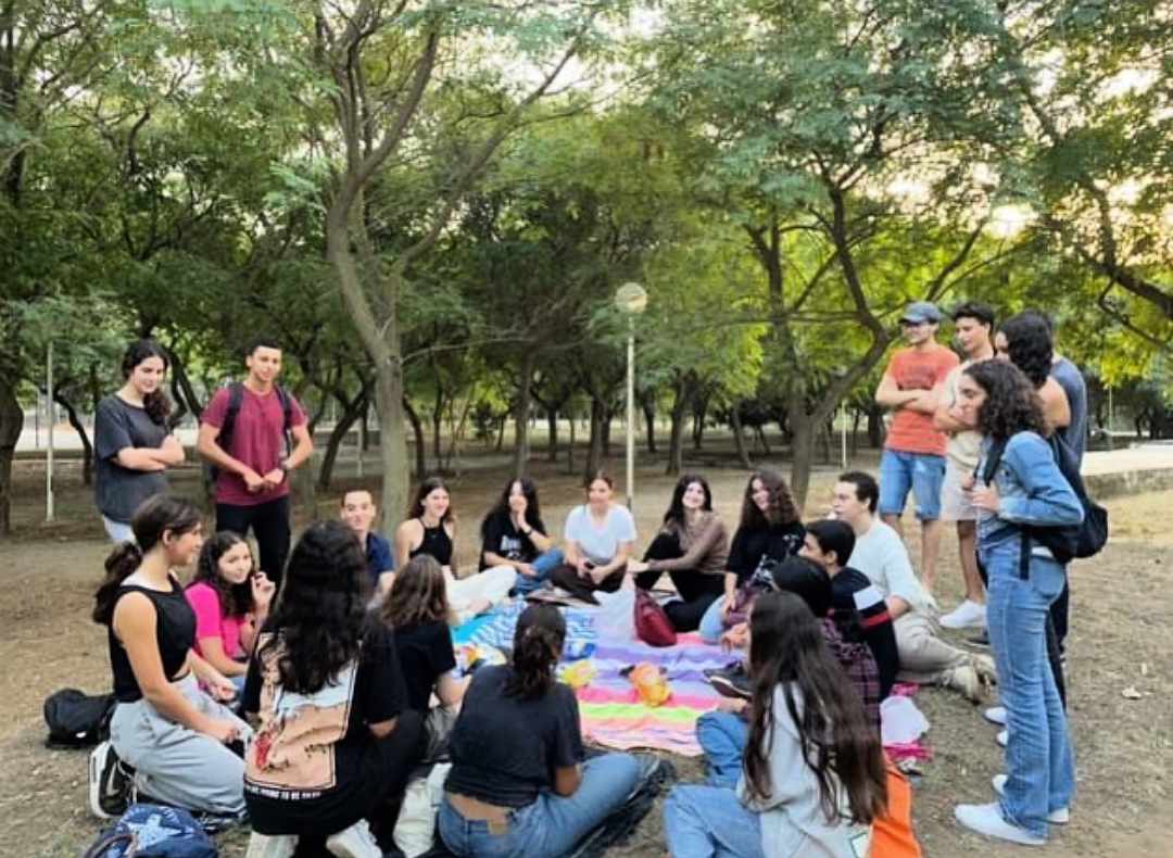 A group gathered around a picnic table beneath trees.