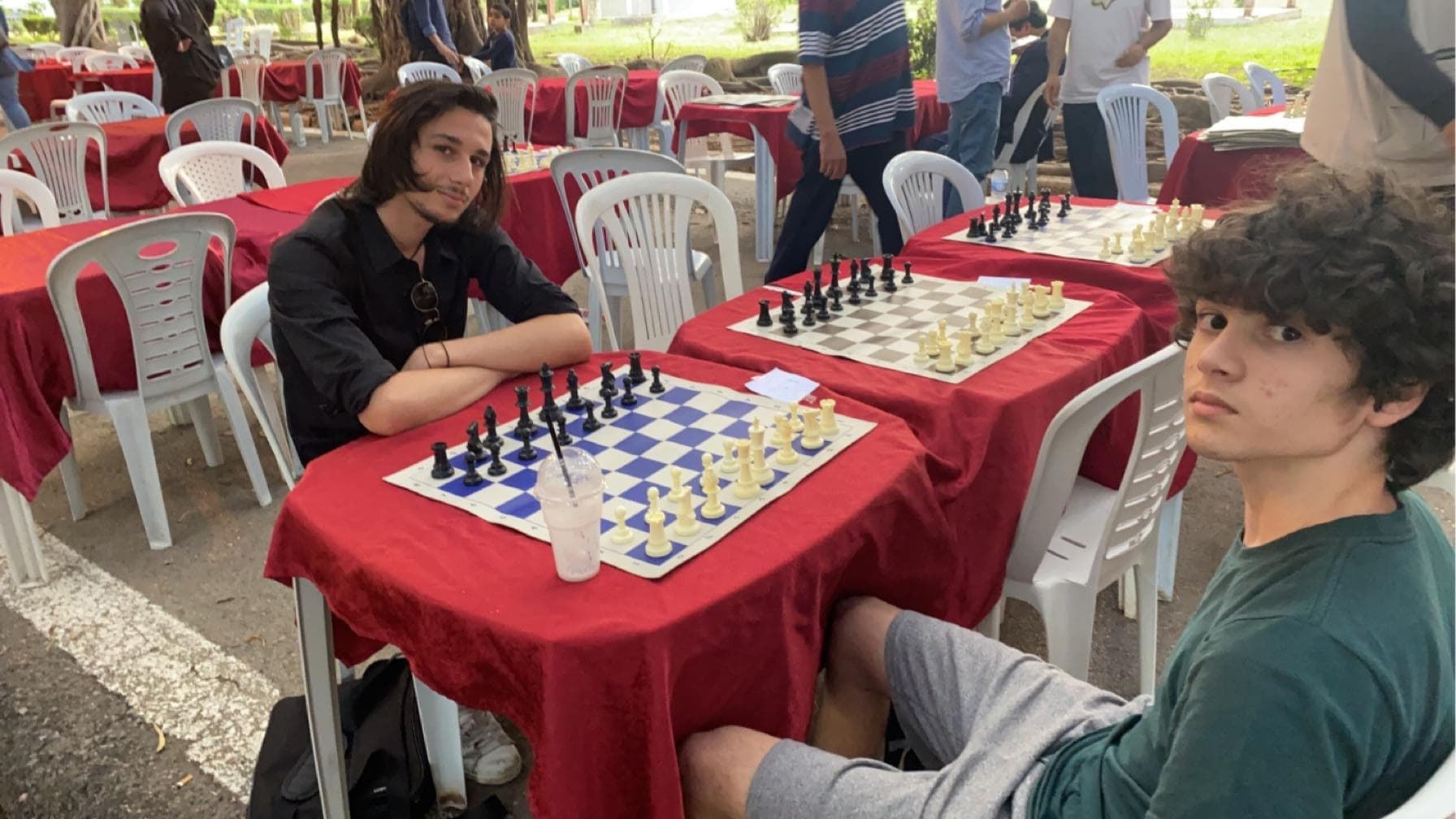 Two players seated at a chessboard on a red-covered table.