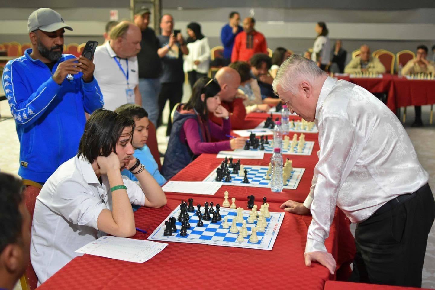 Players seated at chessboards while another person leans over a table.