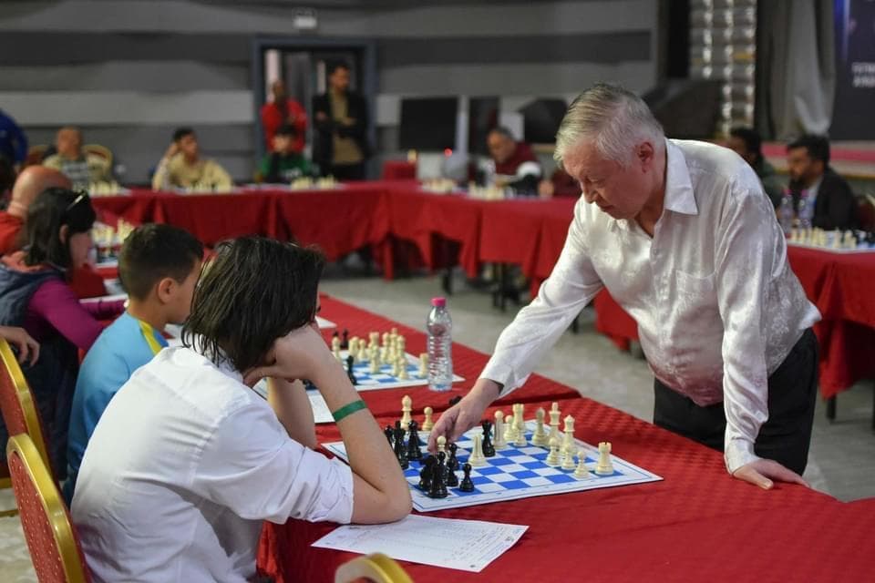 People gathered around chessboards on red-covered tables.