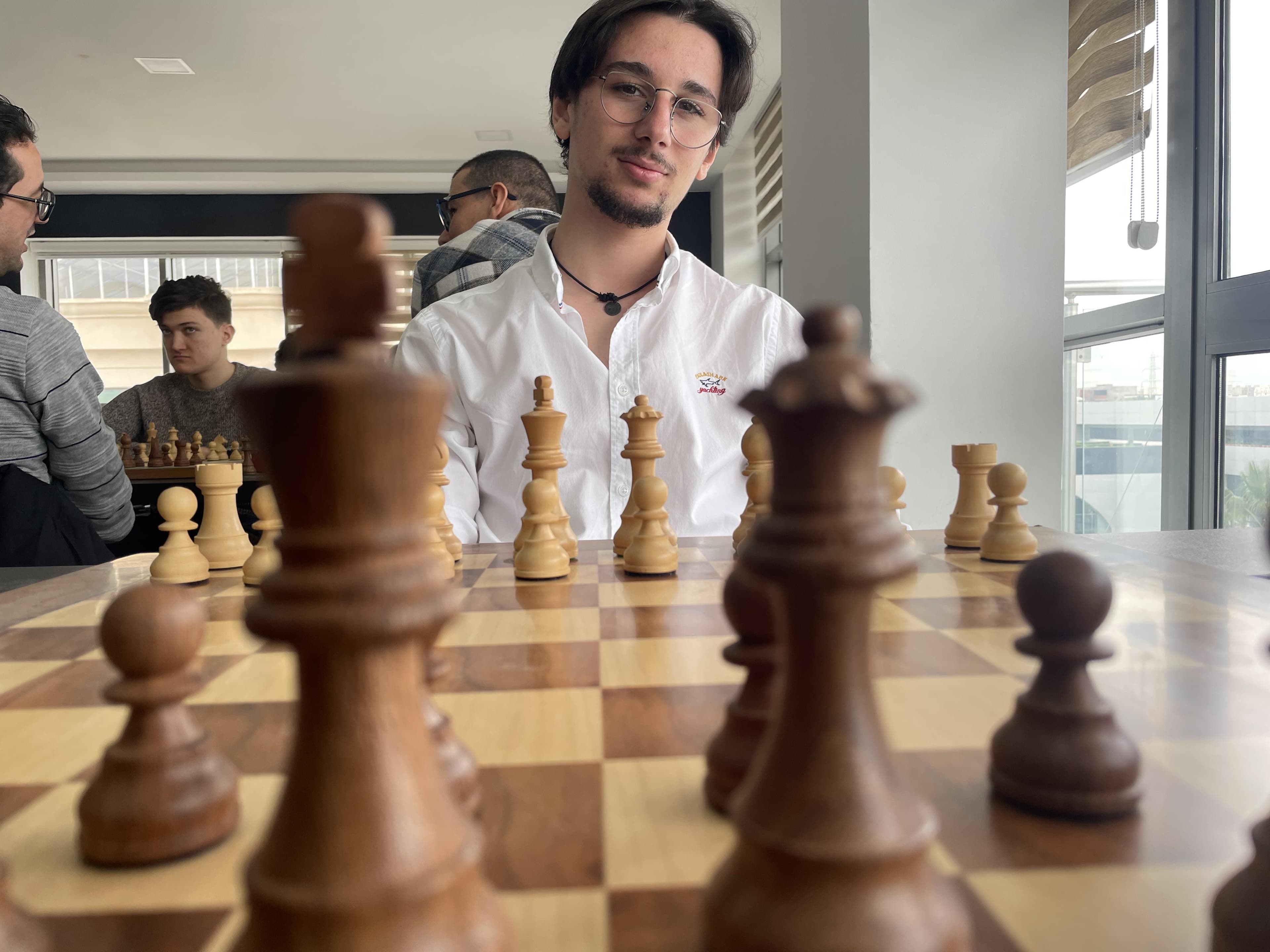 A chessboard in the foreground with a player seated behind it.