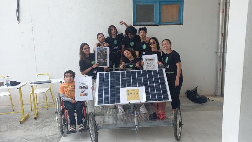 A group posing behind a solar panel mounted on a wheeled frame.