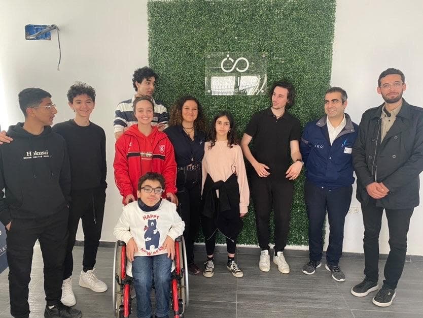 A group posing indoors beside a green wall.