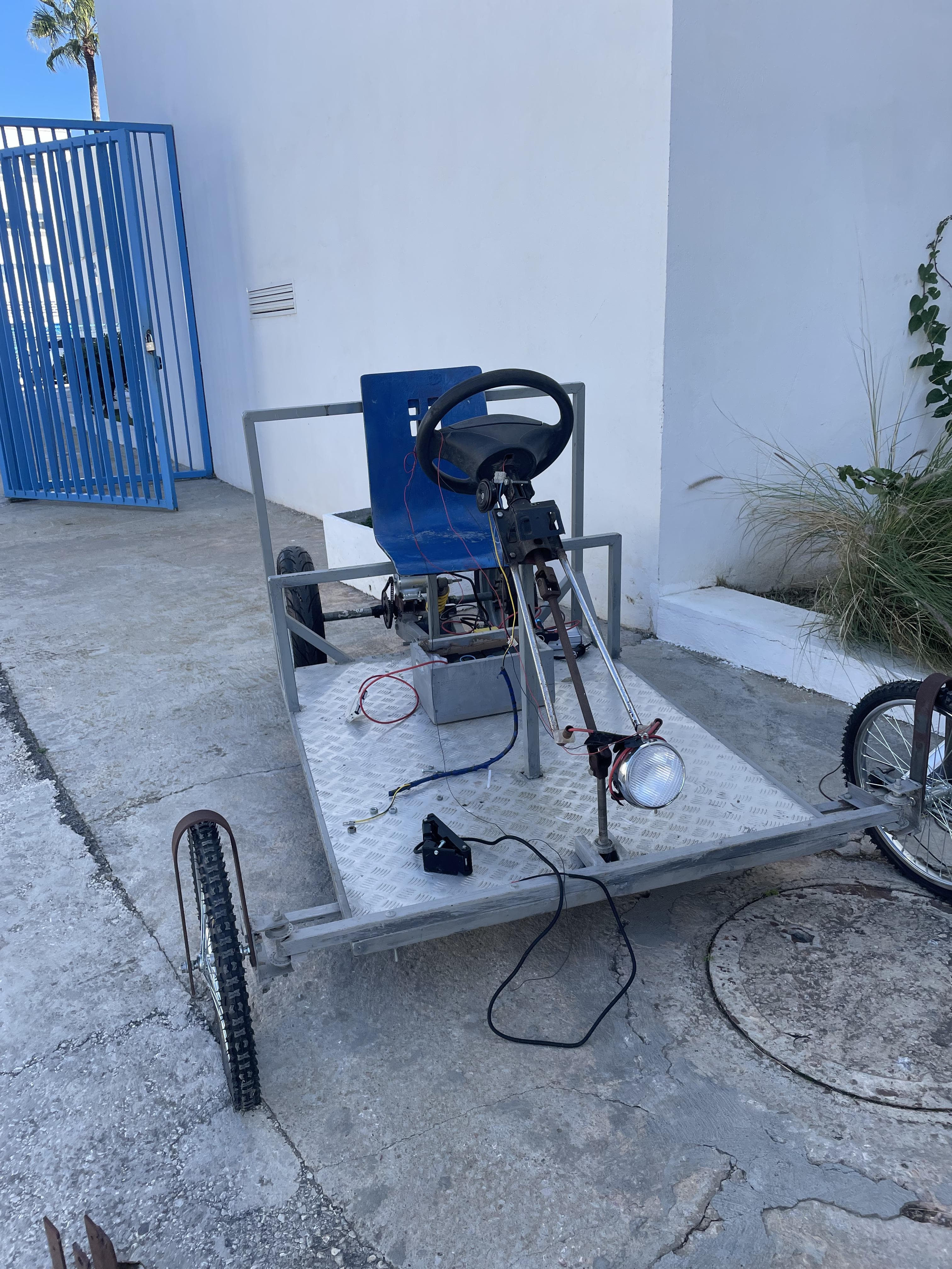 A wheeled metal frame with a steering wheel outside a building.