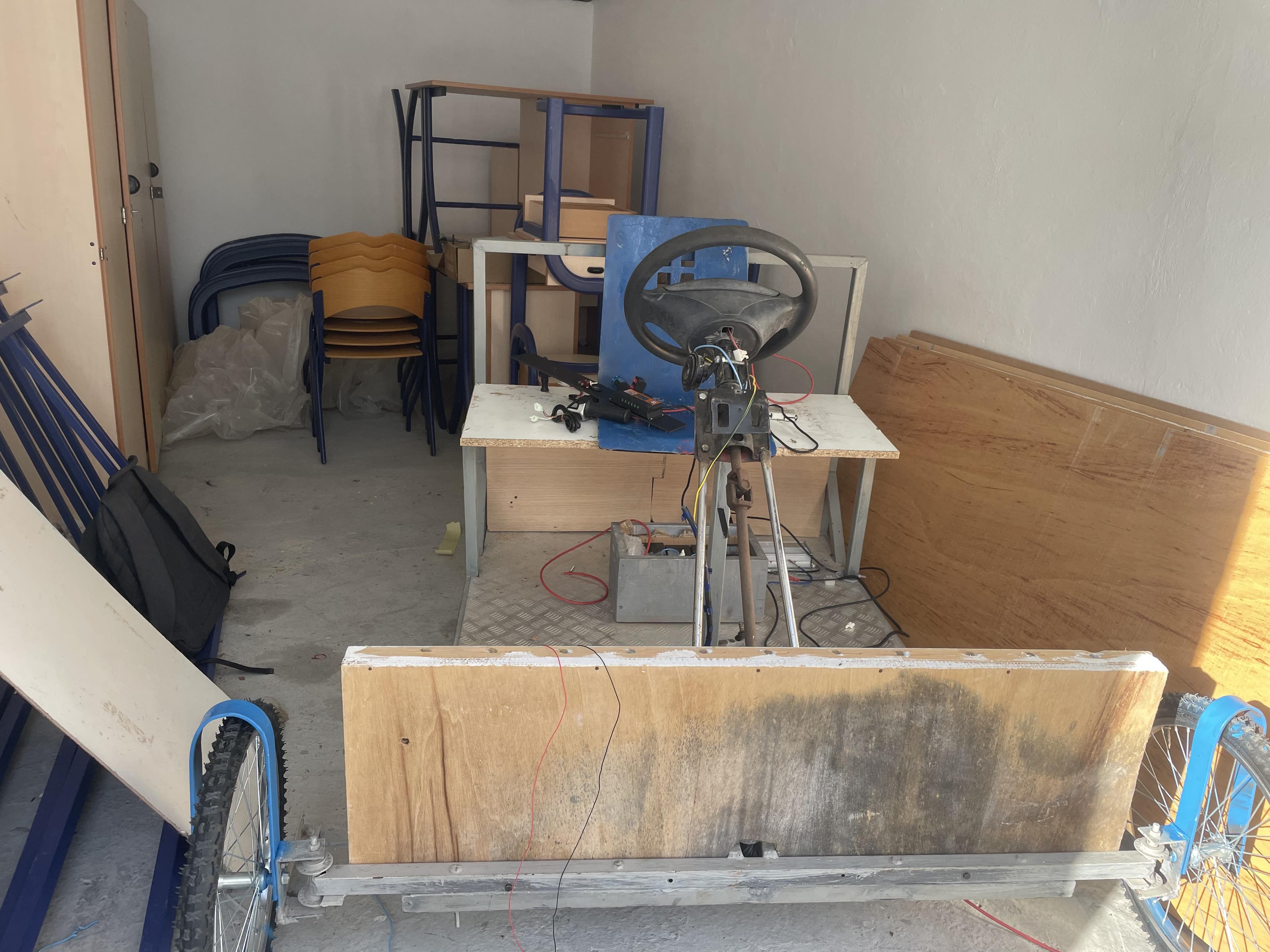 A metal vehicle frame with a steering wheel in a room.