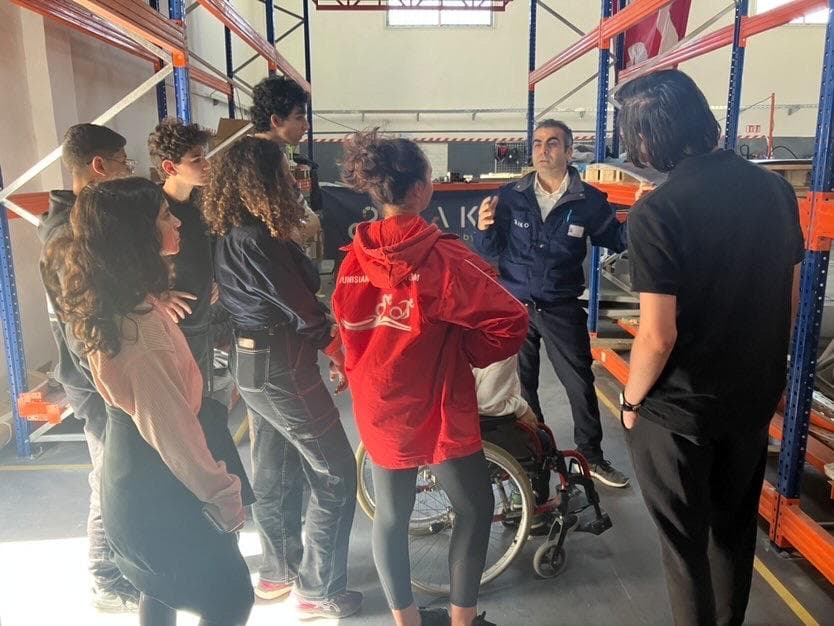 A group gathered around a wheeled metal frame in a workshop.