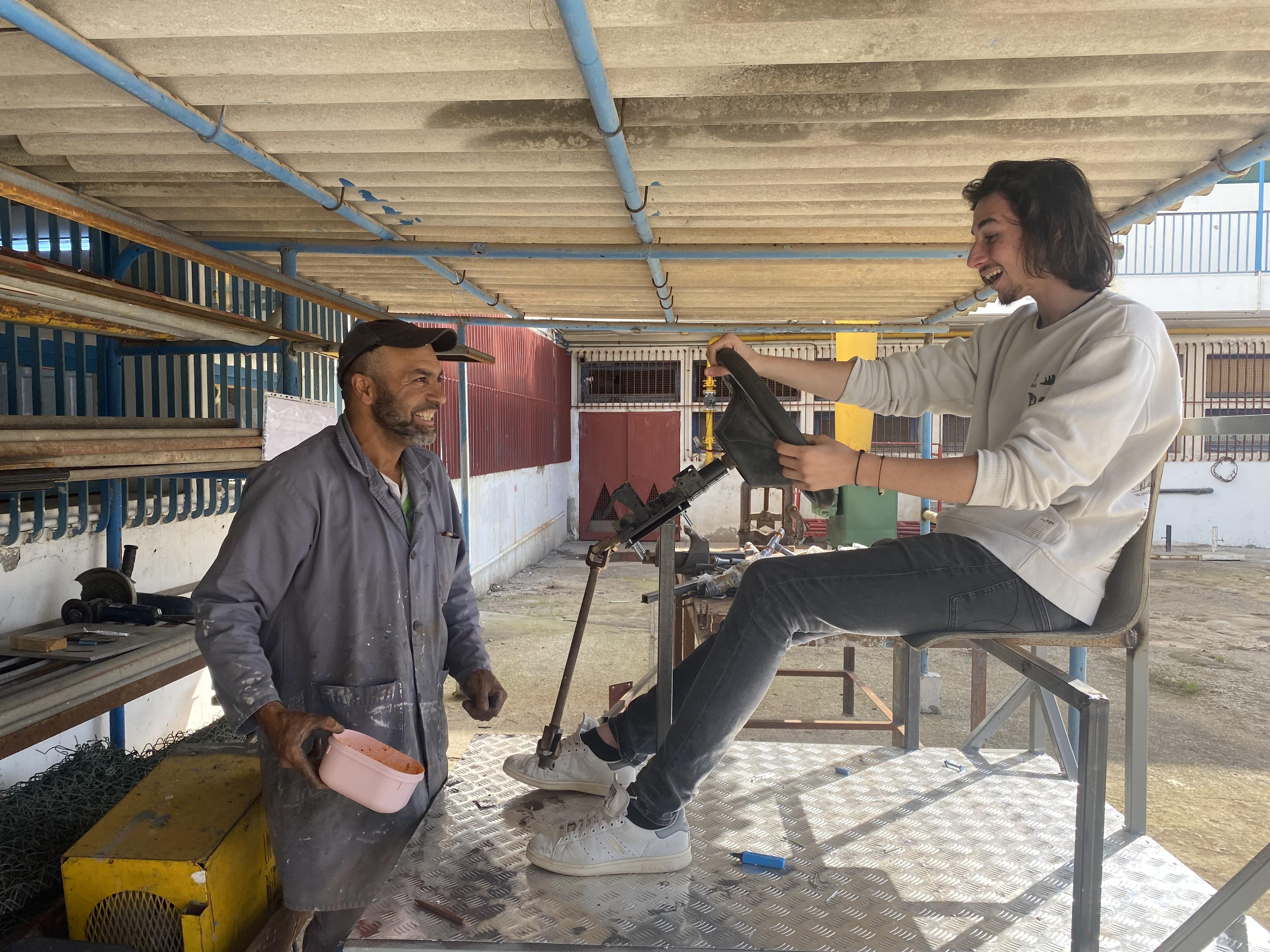 Two people examining a steering wheel on a metal frame.