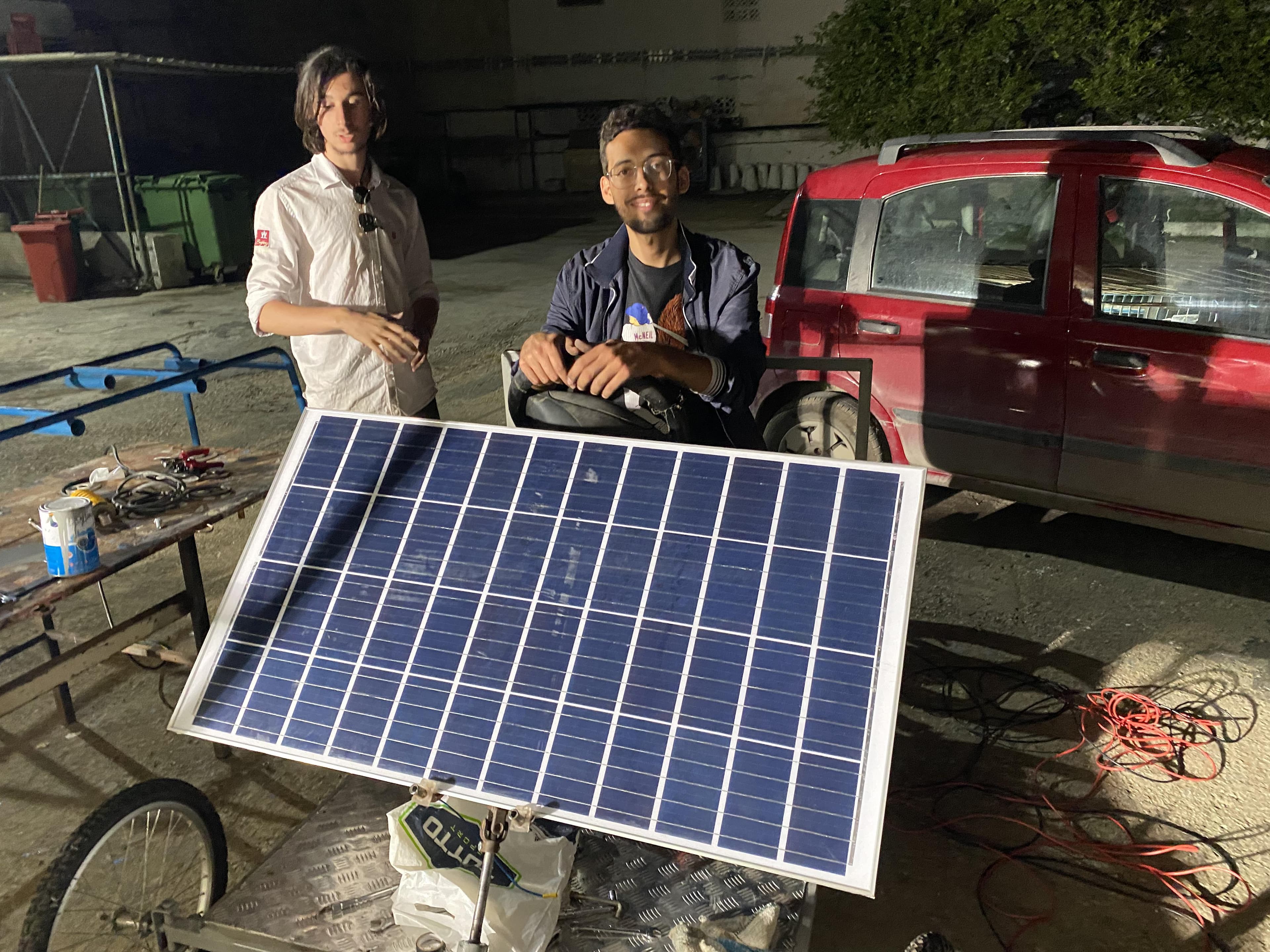 Two people standing behind a solar panel mounted on a wheeled frame.