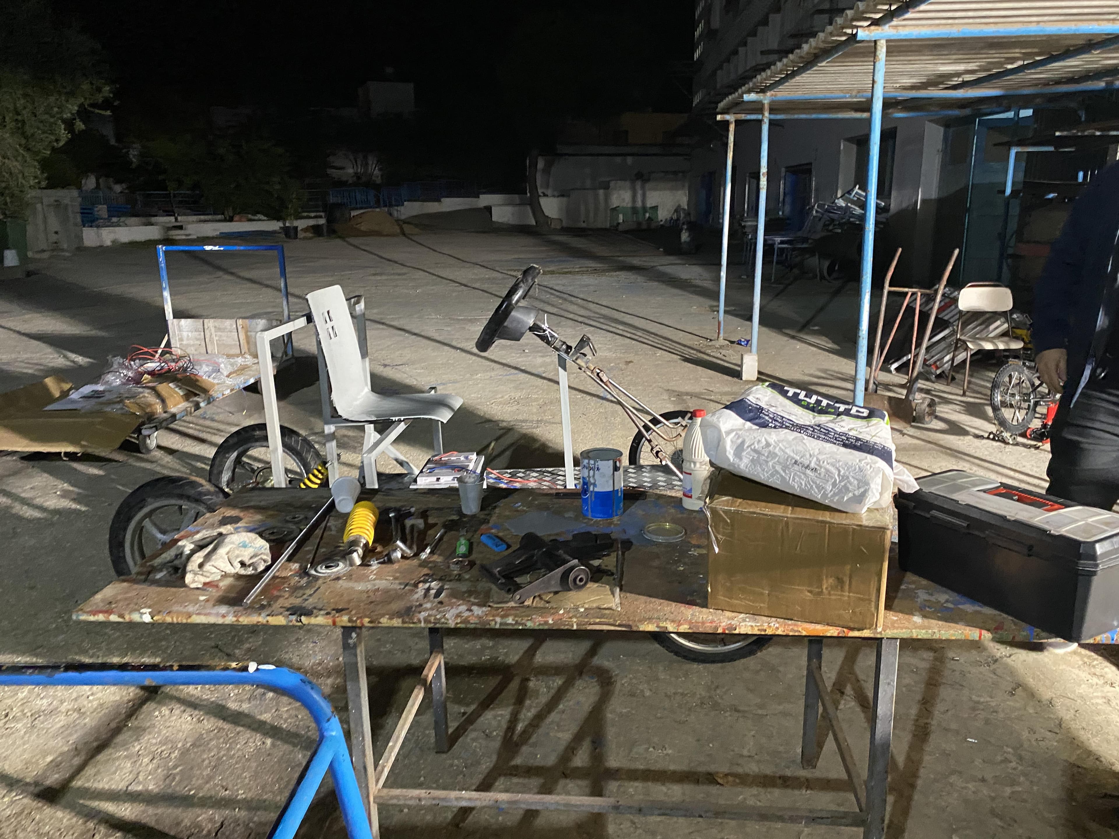 Metal frames, wheels and tools laid out in an outdoor work area.