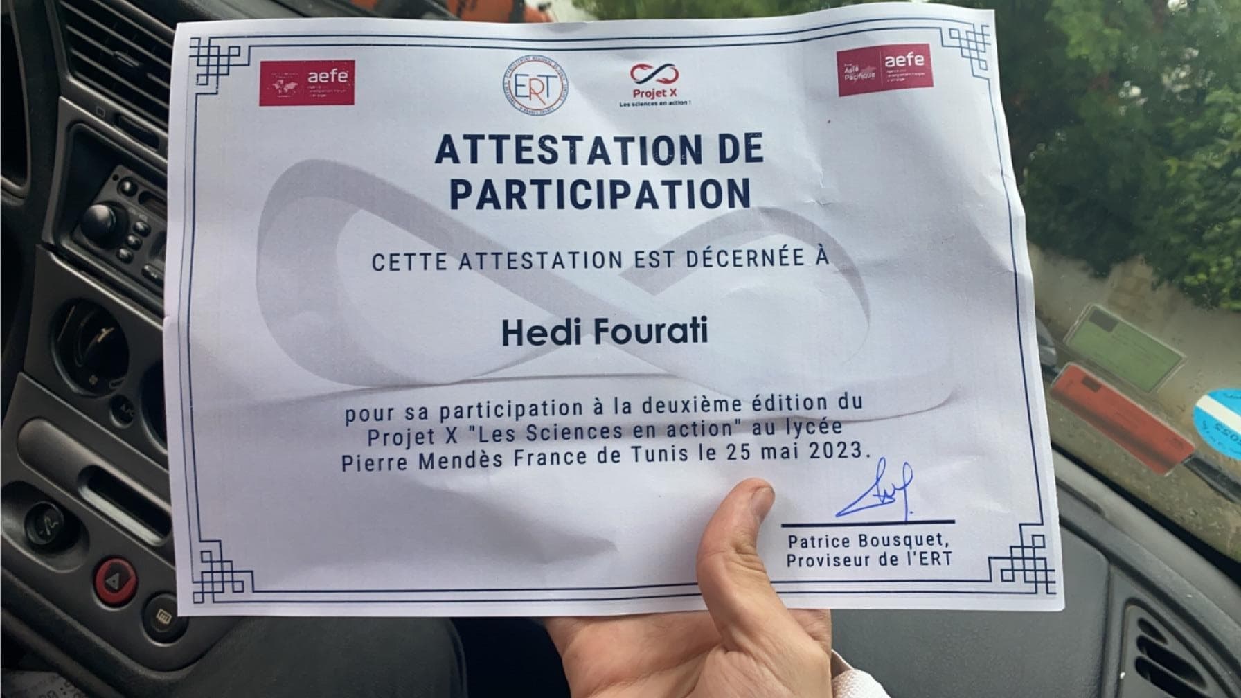 A participation certificate held in front of a steering wheel.