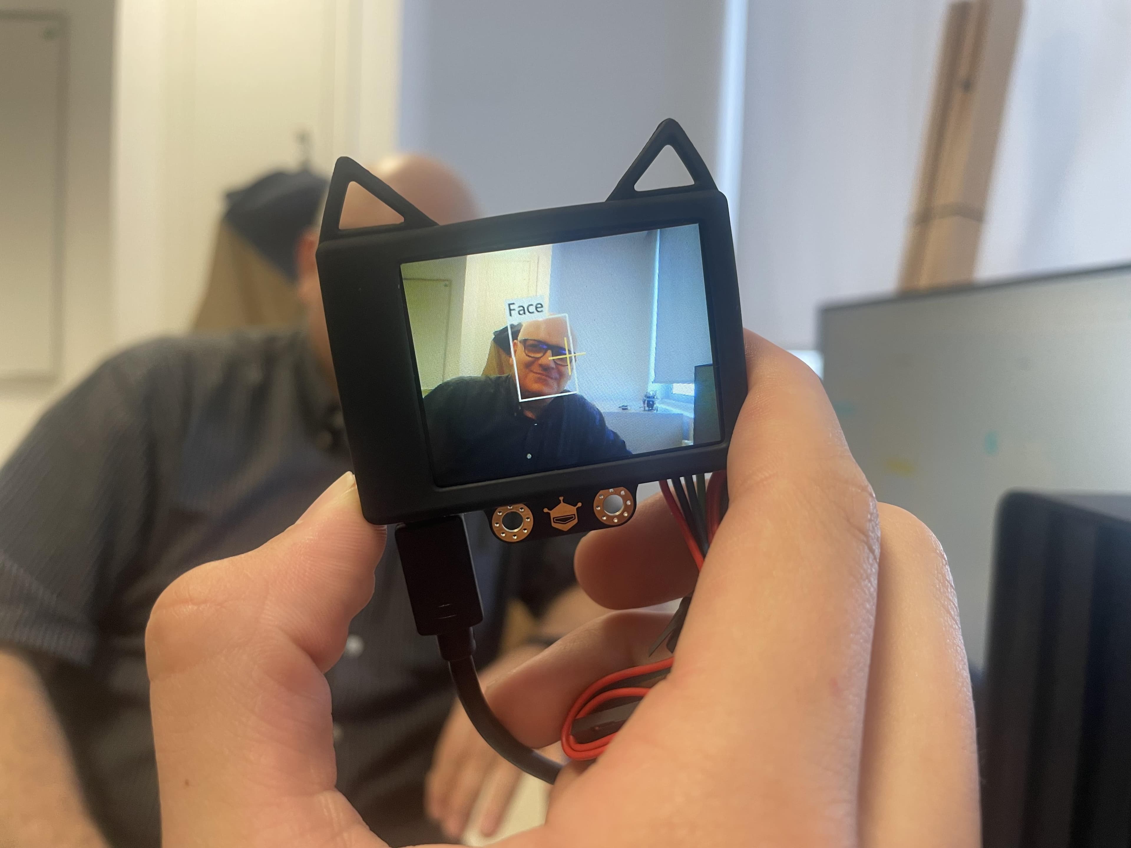 A handheld electronic device showing a person's face on its screen.
