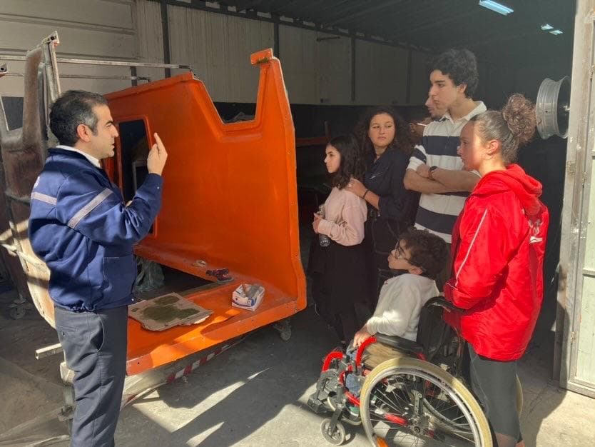 People examining an orange vehicle body in a workshop.