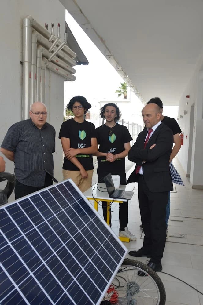 Two people in engineering club shirts beside the solar car and visitors