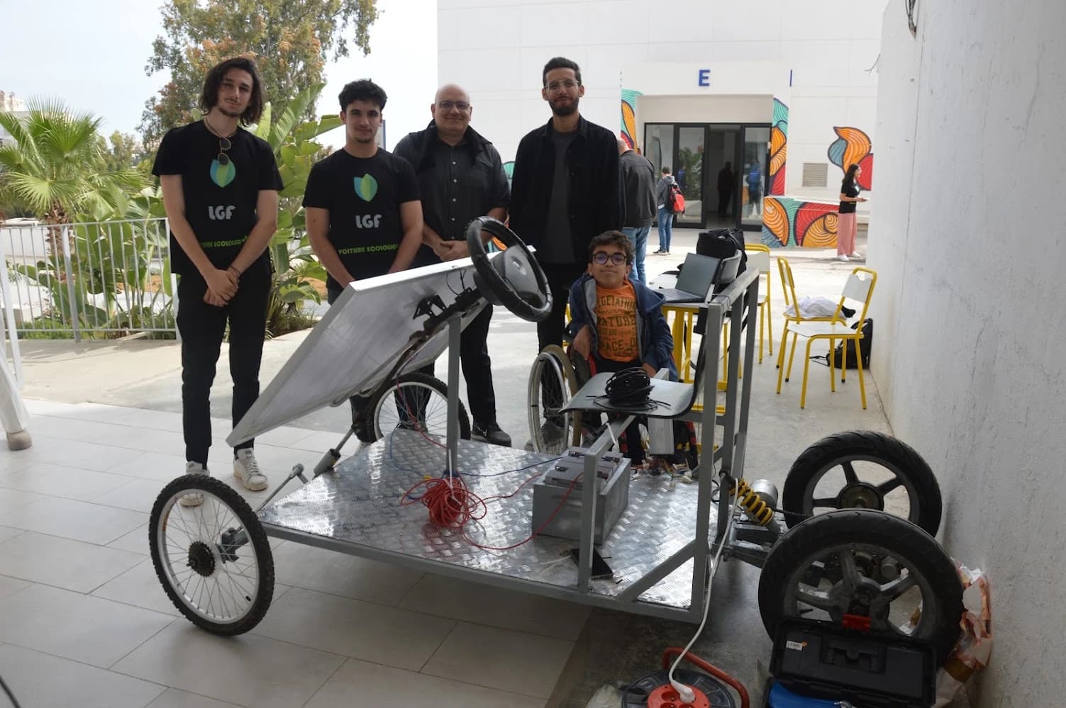 A group beside the solar-electric vehicle, showing its chassis, seat, steering wheel and solar panel