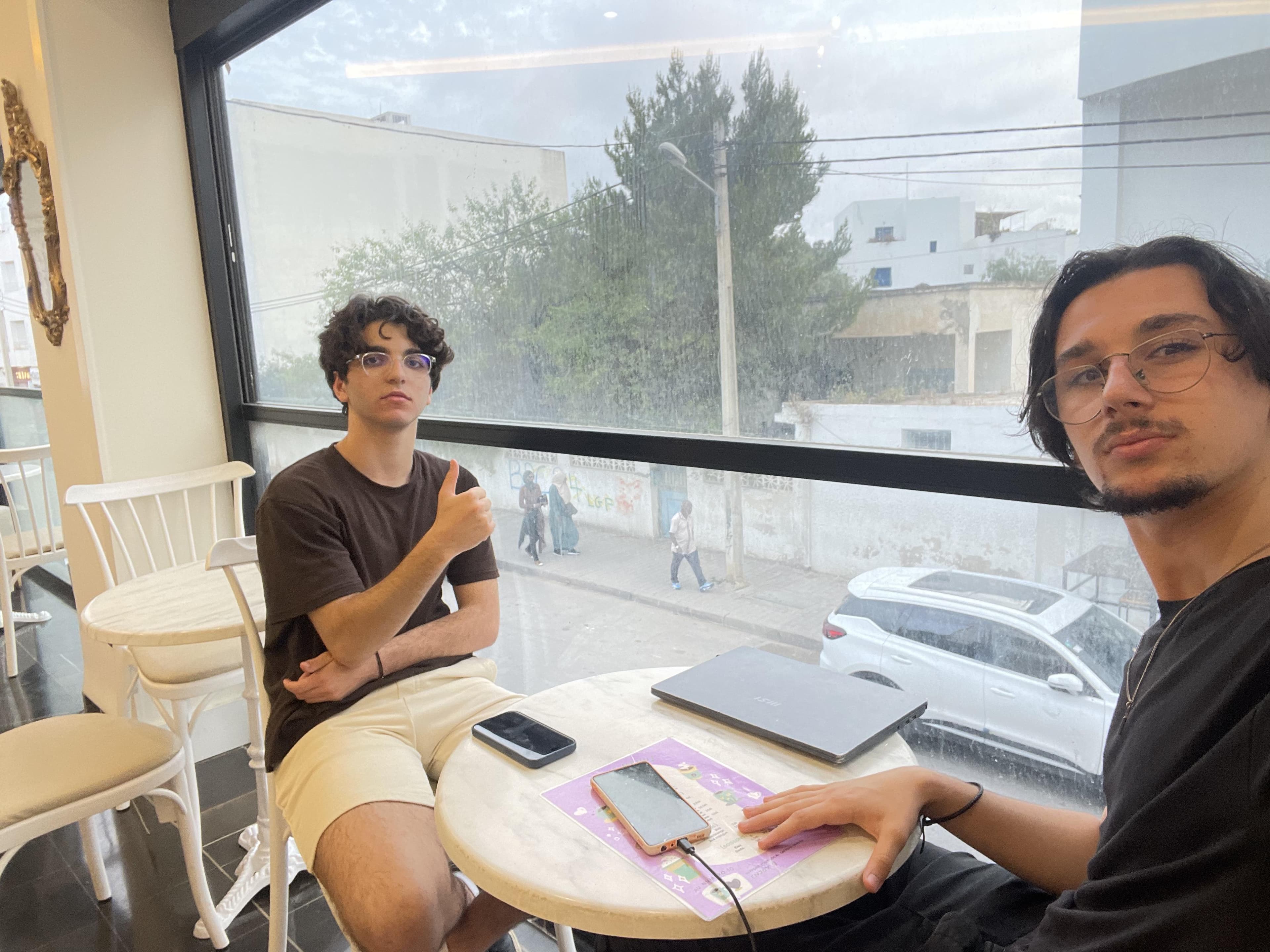 Two people at a table with a tablet beside a window.