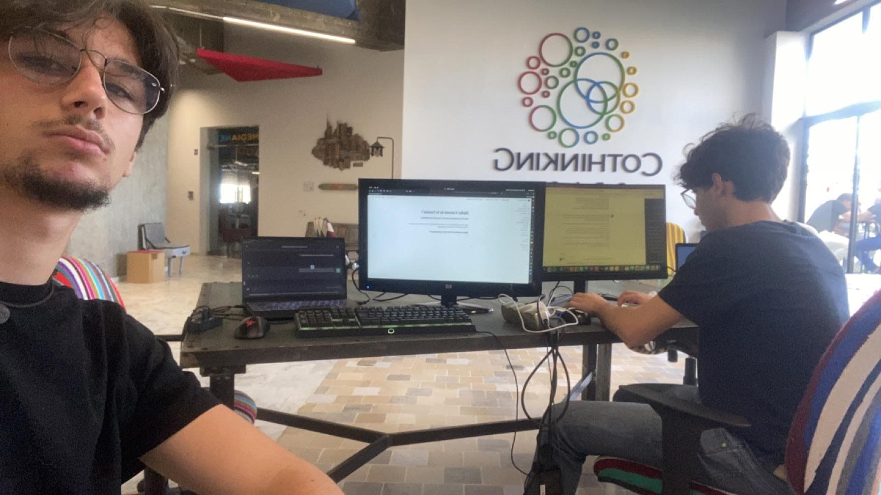 Two people working at a desk with a large monitor.